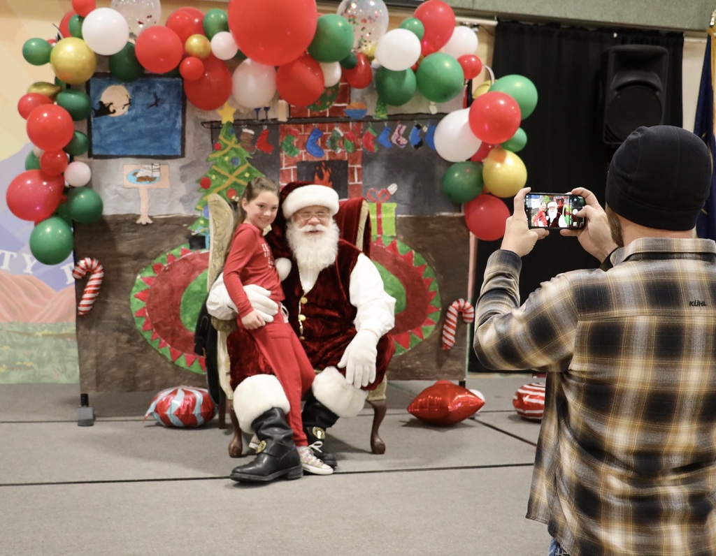 A parent takes a picture of his daughter visiting Santa.